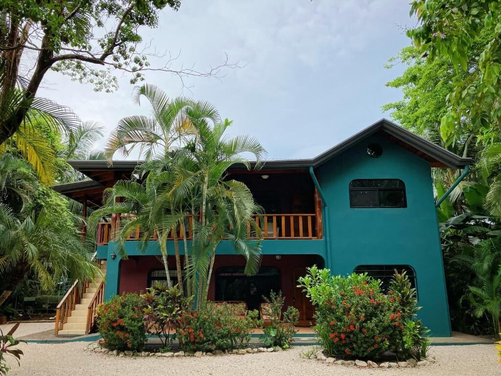 Un edificio de dos pisos con balcón, rodeado de vegetación tropical.