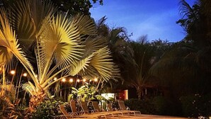 A poolside area with lounge chairs, palm trees, and string lights. - Villa Tortuga Nosara (Playa Guiones)