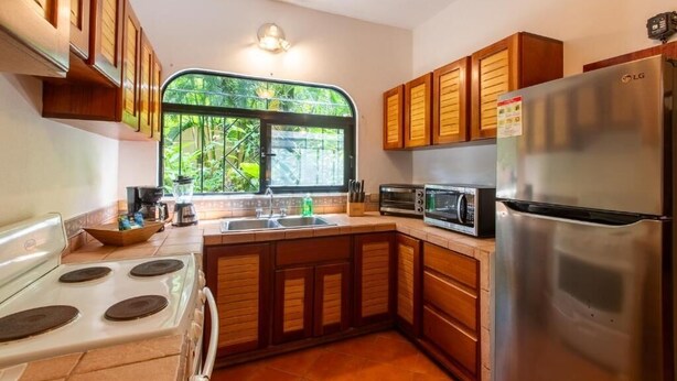 A kitchen with wooden cabinets, a stainless steel refrigerator, a microwave, and a stove. - Villa Tortuga Nosara (Playa Guiones)
