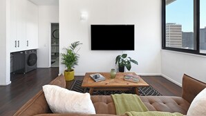 Ein modernes Wohnzimmer mit Flachbildfernseher, einer Couch, einem Couchtisch und Blick auf die Stadt.