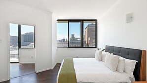 Ein Schlafzimmer mit einem großen Bett, einem Fenster mit Blick auf die Stadt und einer Tür zu einem Außenbereich.