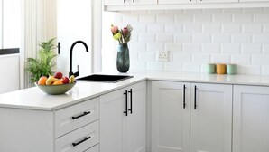 Eine moderne Küche mit weißen Schränken, einem schwarzen Wasserhahn, einer Obstschale und einer Vase mit Blumen.