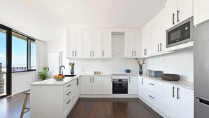 Eine moderne Küche mit weißen Schränken, einer eingebauten Mikrowelle und einem großen Fenster mit Blick auf die Stadt.