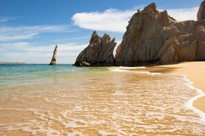 A beach with clear water, a sandy shore, and rocky formations. - Nauti Baja- Condo at The Marina/Near the Beach! (Cabo San Lucas)