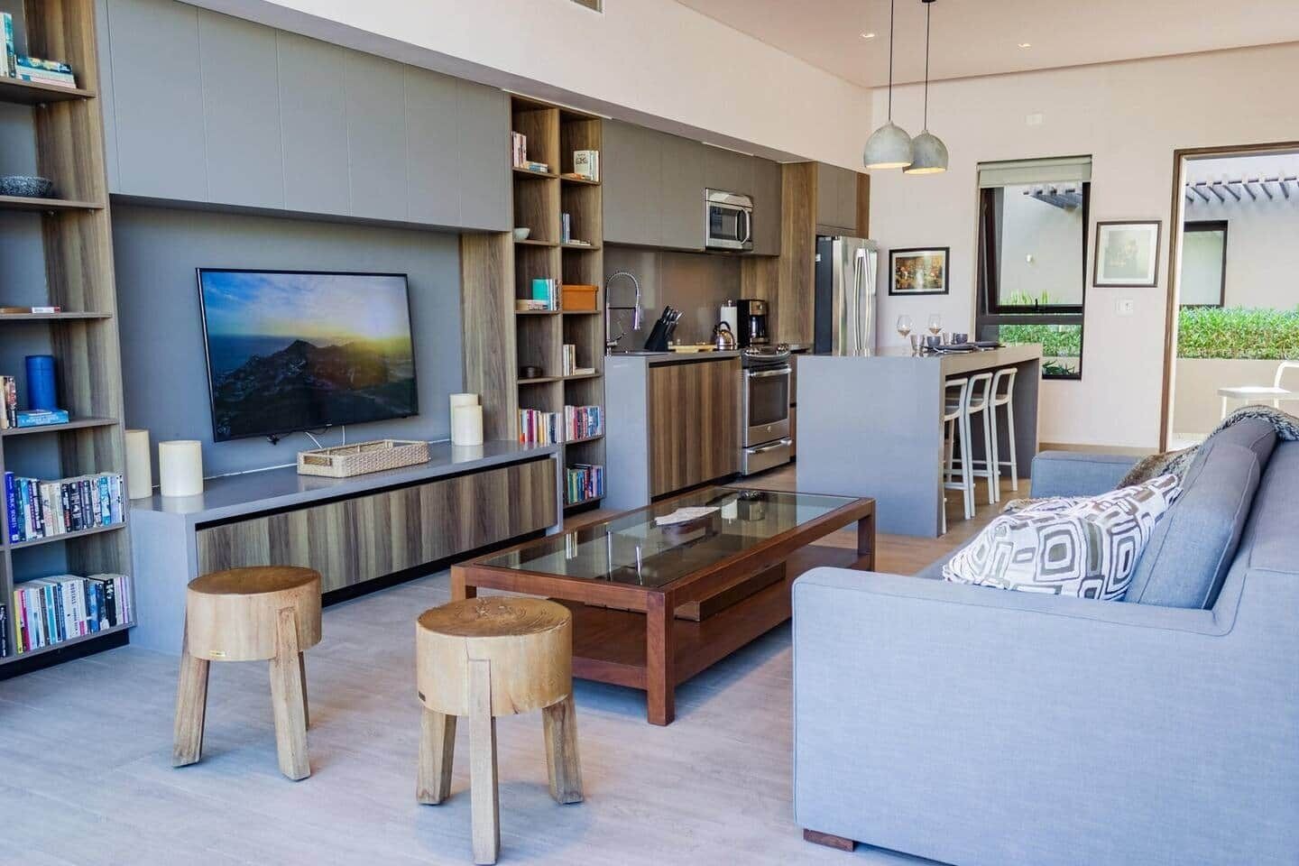 A modern living room with a large flat-screen TV, wooden bookshelves, a glass coffee table, and a grey sofa.