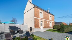 A two-story house with a brick exterior, a front porch, and a patio area with outdoor furniture. - Gîtes de France® - Authenticity and modernity (CUVERVILLE SUR YERES)