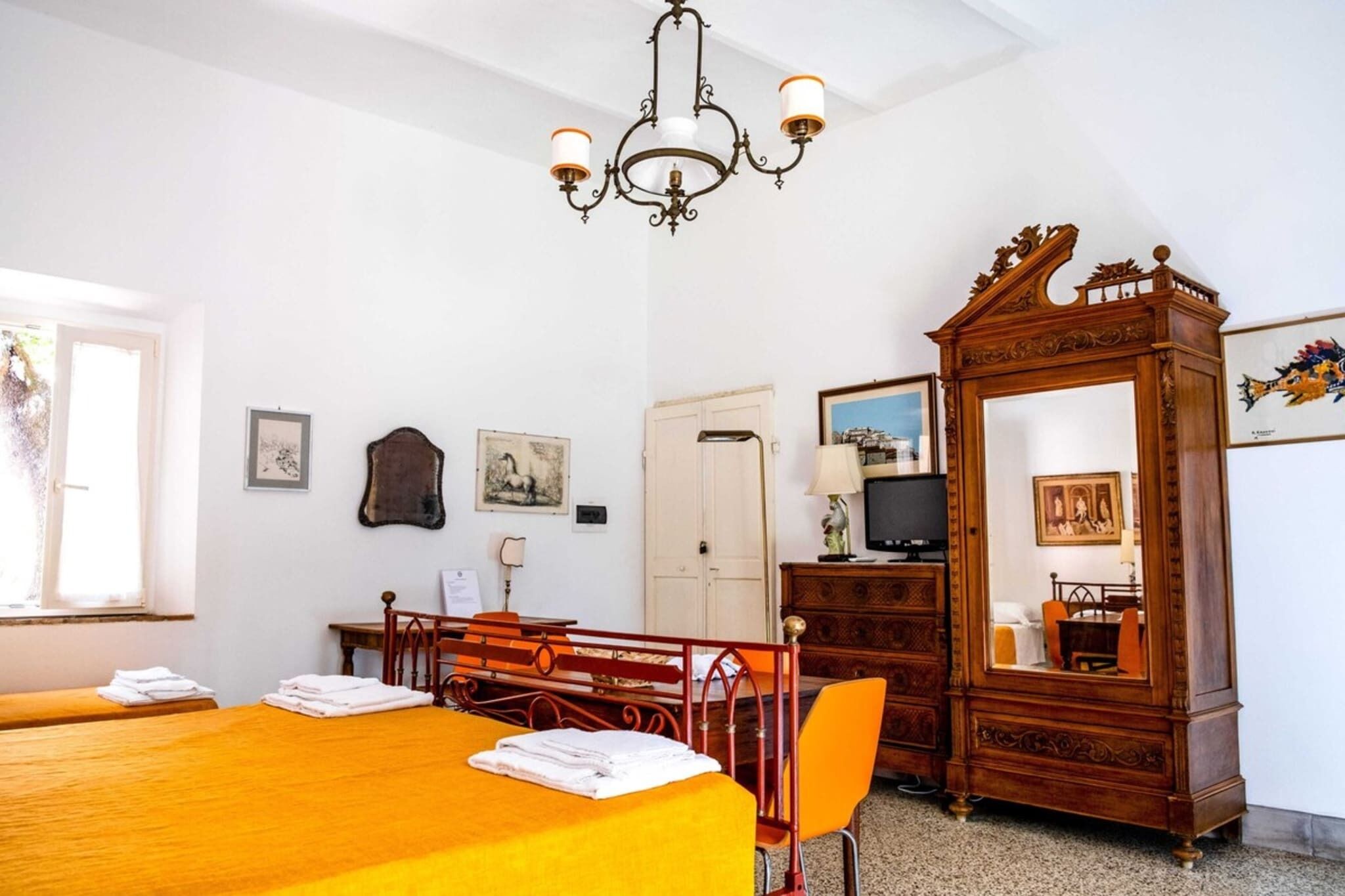 A hotel room with a wooden dining table, a chandelier, a television, and a large mirror.