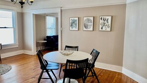 A dining area with a round table, four chairs, a chandelier, and three framed artworks on the wall.