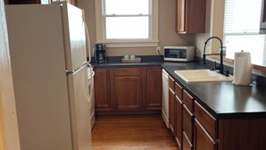 A kitchen with wooden cabinets, a refrigerator, a microwave, a sink, and a window.