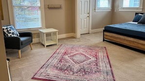 A bedroom with a bed, a chair, a small table, a rug, and a door.