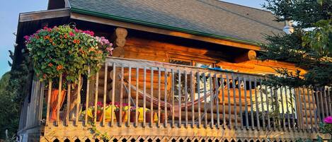 A wooden cabin with a porch, a hammock, and a lattice fence.