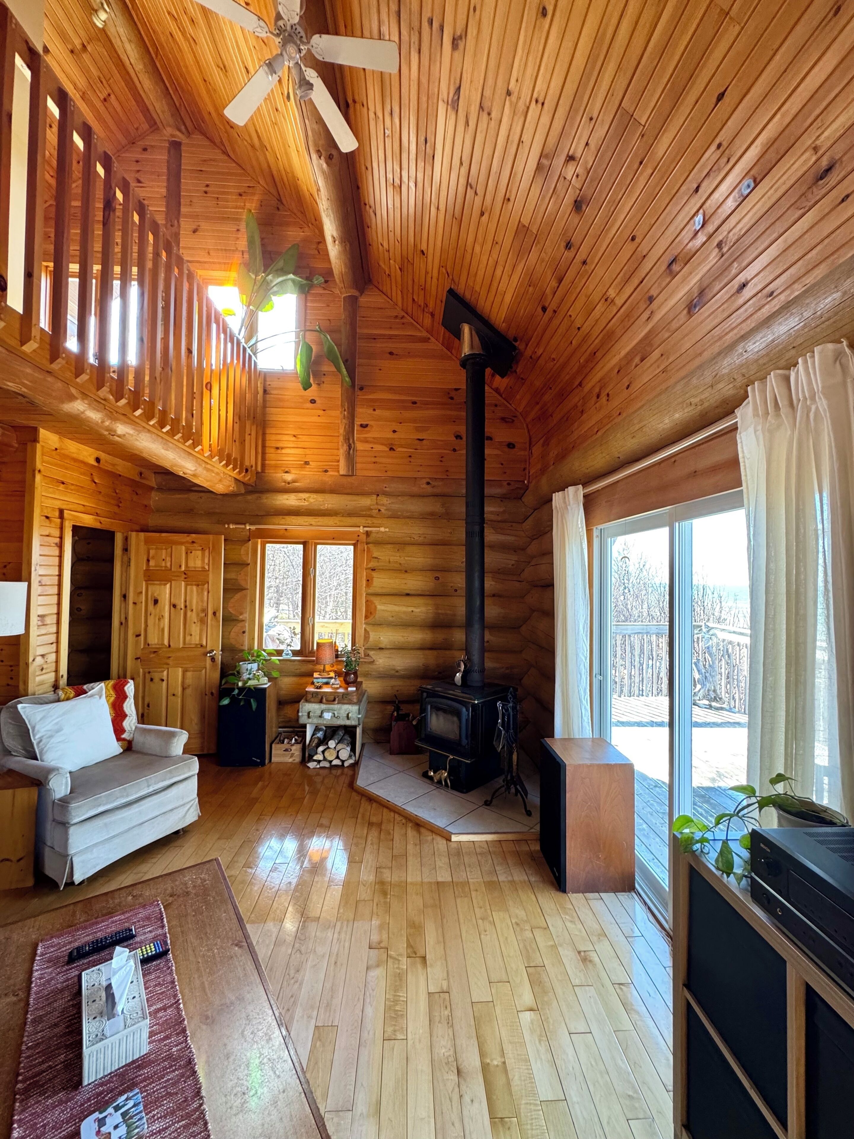 Ein Interieur einer Blockhütte mit Kamin, Holzböden, einer Couch, einem Fernsehmöbel und einem Balkon mit Blick.