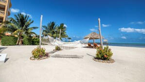 A beach resort with a hammock, palm trees, a thatched-roof structure, and a view of the ocean. - Oceans Edge Resort & Spa (San Pedro)