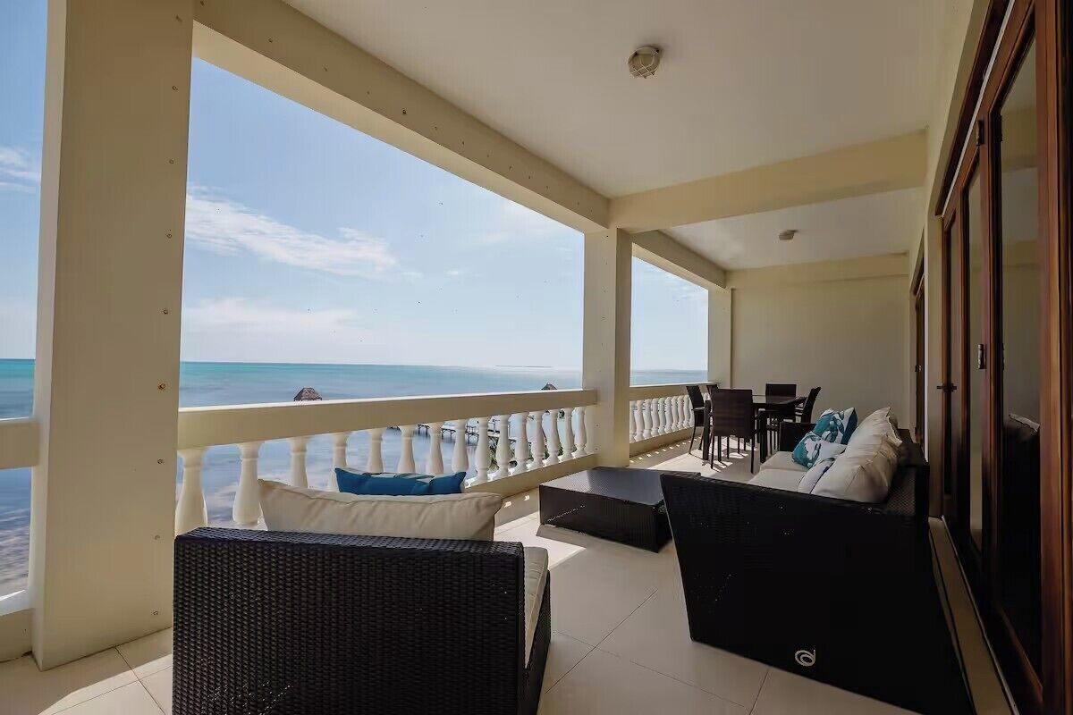 A balcony with a view of the sea, furnished with wicker chairs and a sofa, and a dining table.