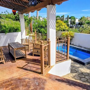 Eine überdachte Terrasse mit Holzmöbeln, einem Pool und umgebender Bepflanzung.