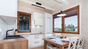 A modern kitchen with wooden cabinets, a sink, and a dining area with a table and chairs. - Comfortable Holiday Home , Summer Pool (Rewal)