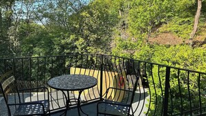 Ein Balkon mit rundem Tisch und Stühlen, umgeben von einem Metallgeländer, mit Blick auf eine üppige Grünfläche.