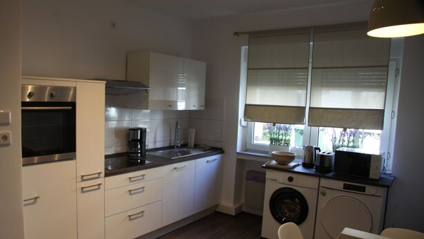 A compact kitchen with a washing machine, a microwave, and a coffee maker. - Work Inn Rhein Ruhr Apartment (Duisburg)