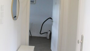 A hallway with a white wall, a door on the right, and a mirror on the left. - Work Inn Rhein Ruhr Apartment (Duisburg)