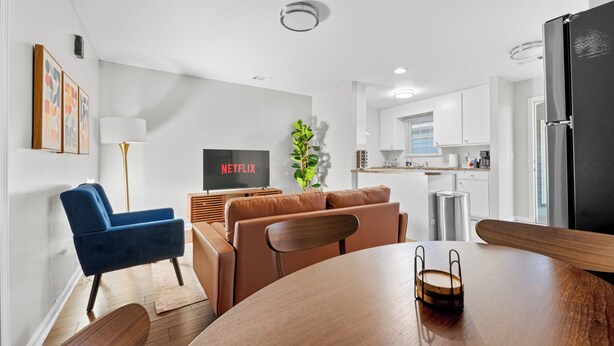 A modern living room with a TV, sofa, dining table, and kitchen in the background. - 1Br 1Bath Long Stays Near Fort Moore (Columbus)