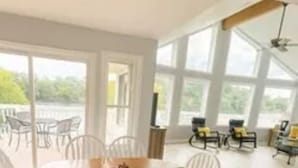 A spacious dining area with a wooden table and white chairs, large windows, and a high ceiling. - Lakefront Escape: hot tub, endless views, deep water dock, gentle walk to water (Goodview)
