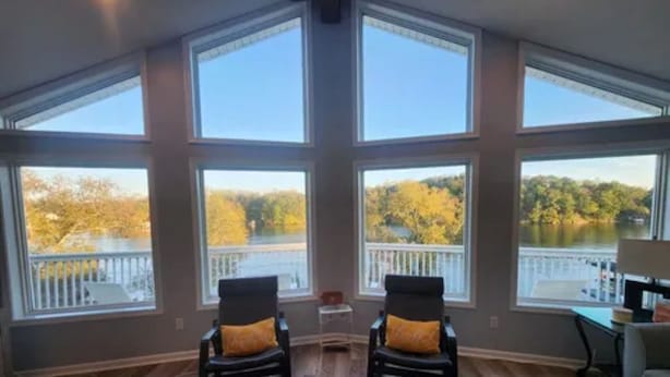 A room with large windows, two chairs, a table, and a view of a lake. - Lakefront Escape: hot tub, endless views, deep water dock, gentle walk to water (Goodview)
