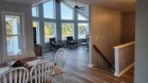 A spacious room with a dining area, large windows, and a staircase. - Lakefront Escape: hot tub, endless views, deep water dock, gentle walk to water (Goodview)