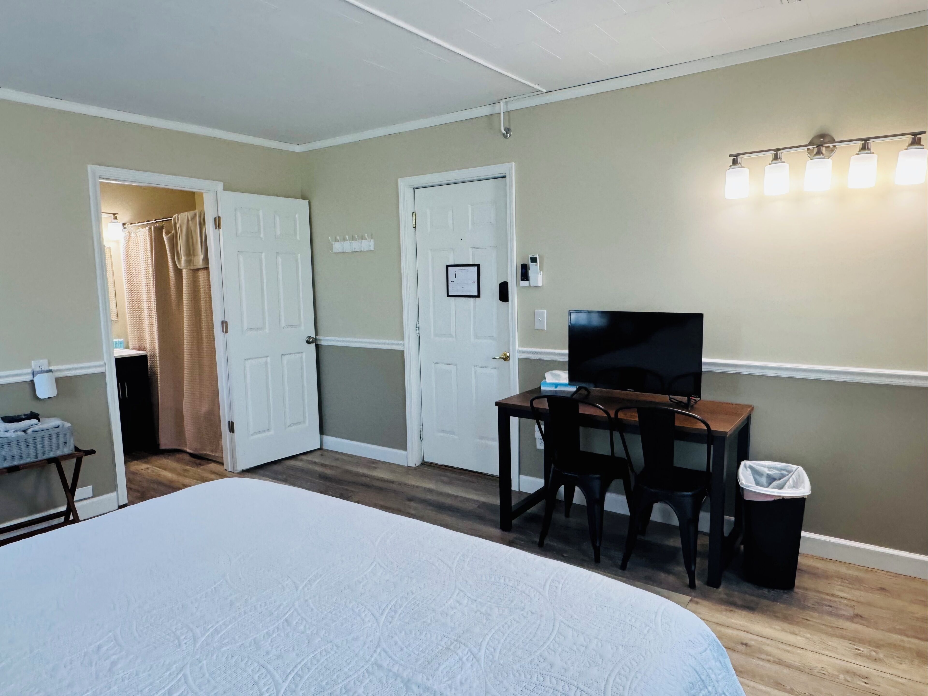 Une chambre d’hôtel avec un lit, un bureau avec deux chaises, une télévision et une salle de bain visible à travers une porte ouverte.