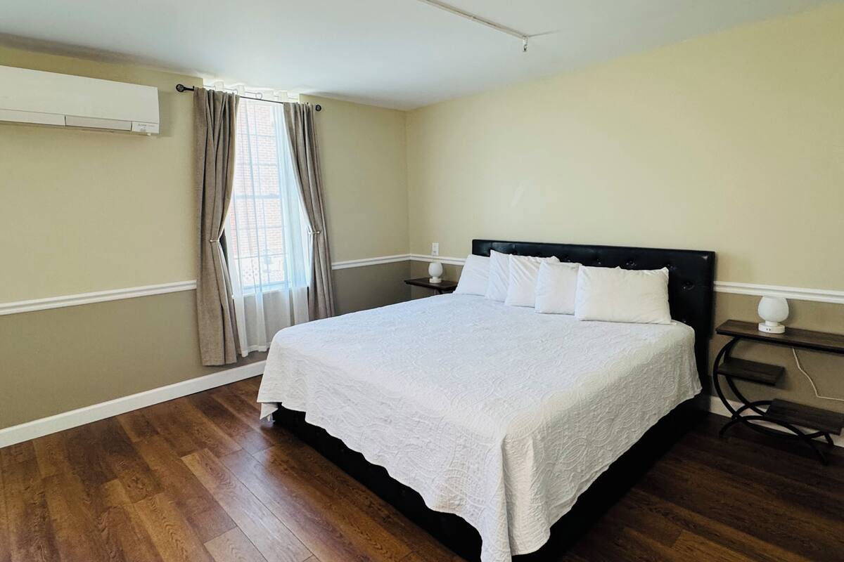 Una camera da letto con un letto grande, un comodino, una lampada, una finestra con tende e un condizionatore d'aria.