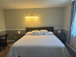 A hotel room with a bed, bedside tables, a chair, and a wall-mounted light fixture. - Nestle Inn (Hermann)