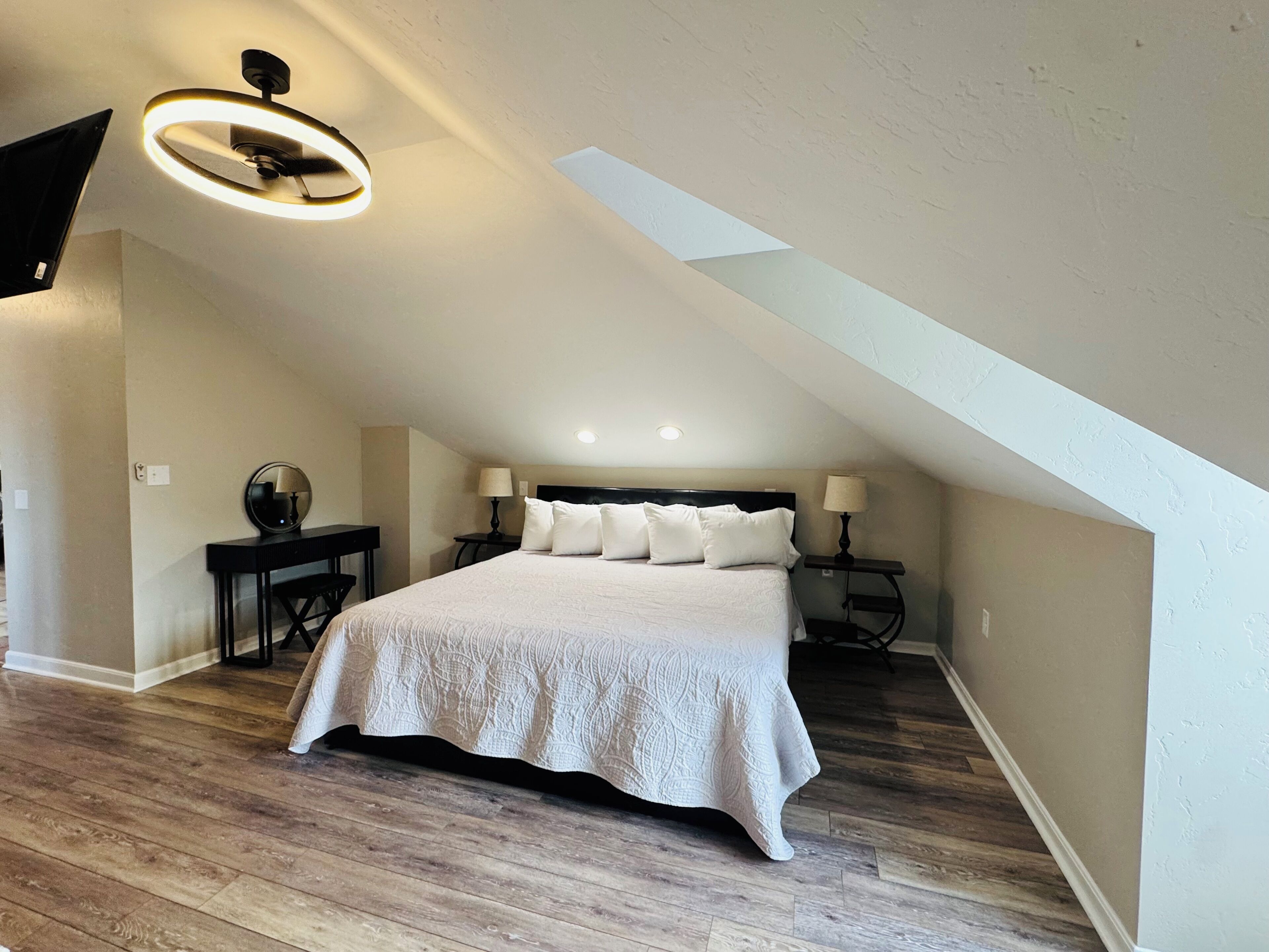 Ein Schlafzimmer mit einem großen Bett, zwei Nachttischen, einem Deckenventilator und einem Oberlicht.