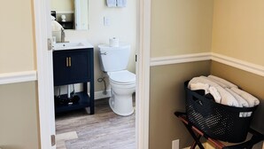 Une salle de bain équipée de toilettes, d’un lavabo, d’un miroir et d’un téléviseur noir fixé au mur.