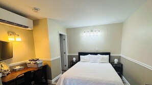 Une chambre à coucher comprenant un lit, des tables de chevet, un bureau avec une chaise, un miroir et un luminaire fixé au mur.