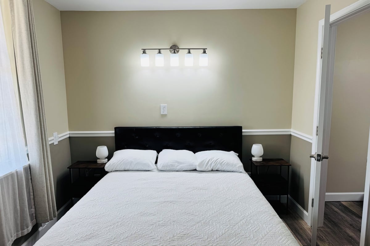 Una camera da letto con un letto, lampade sui comodini, un punto luce a parete e una porta.