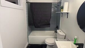 Ein kleines Badezimmer mit Badewanne, Toilette und Waschbecken, mit einem schwarz-weißen Marmorboden und einem kleinen Fenster.