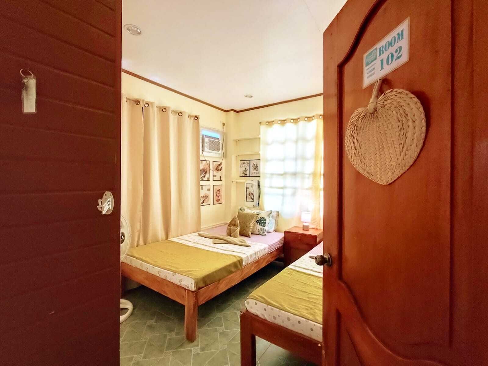 A room with a bed, a bedside table, a wall-mounted air conditioner, and a sign indicating 'ROOM 102'.