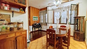 A dining area with a wooden table and chairs, a ceiling fan, and a sign reading 'AMWANI Homestay.' - Amwani Residence - Westville (Puerto Princesa)