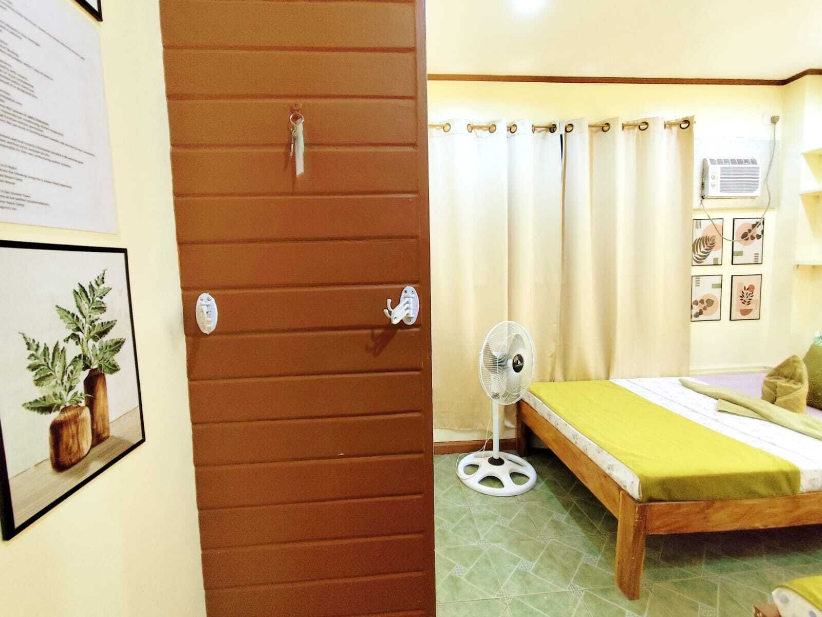 A room with a bed, a standing fan, and a door with a keyhole.