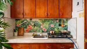 A kitchen with wooden cabinets, a gas stove, and a backsplash with a tropical design. - Amwani Residence - Westville (Puerto Princesa)