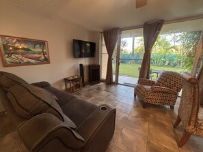 A living room with a sofa, a television, a small table, and a patterned chair. - Adorable 1-bedroom apartment with AC in sunny Kihei (Kihei)