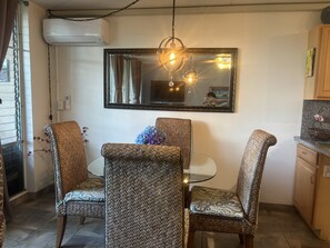 A dining area with wicker chairs, a round table, a mirror, and a hanging light fixture. - Adorable 1-bedroom apartment with AC in sunny Kihei (Kihei)