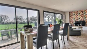 Una sala de estar moderna con comedor, ventanas grandes y televisor.