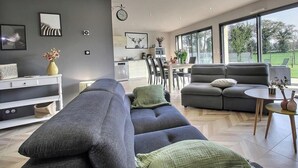 Una sala de estar moderna con un sofá gris, un comedor y ventanas grandes.