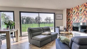Una sala de estar moderna con un sofá gris, un sofá azul, un televisor y un ventanal con vistas a un paisaje verde.