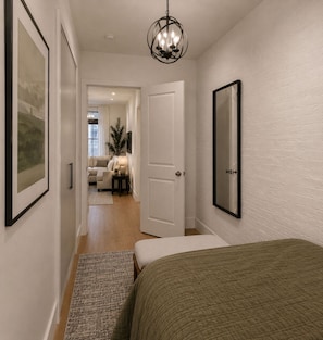 Ein Flur, der zu einem Schlafzimmer führt, mit einem Bett, einer Tür und einem gerahmten Bild an der Wand.