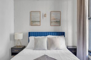 Una cama bien hecha con un cabecero azul, ropa de cama blanca y dos mesitas de noche con lámparas.