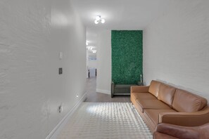 Un pasillo con un sofá de cuero marrón, un tapete texturizado blanco y una pared verde.