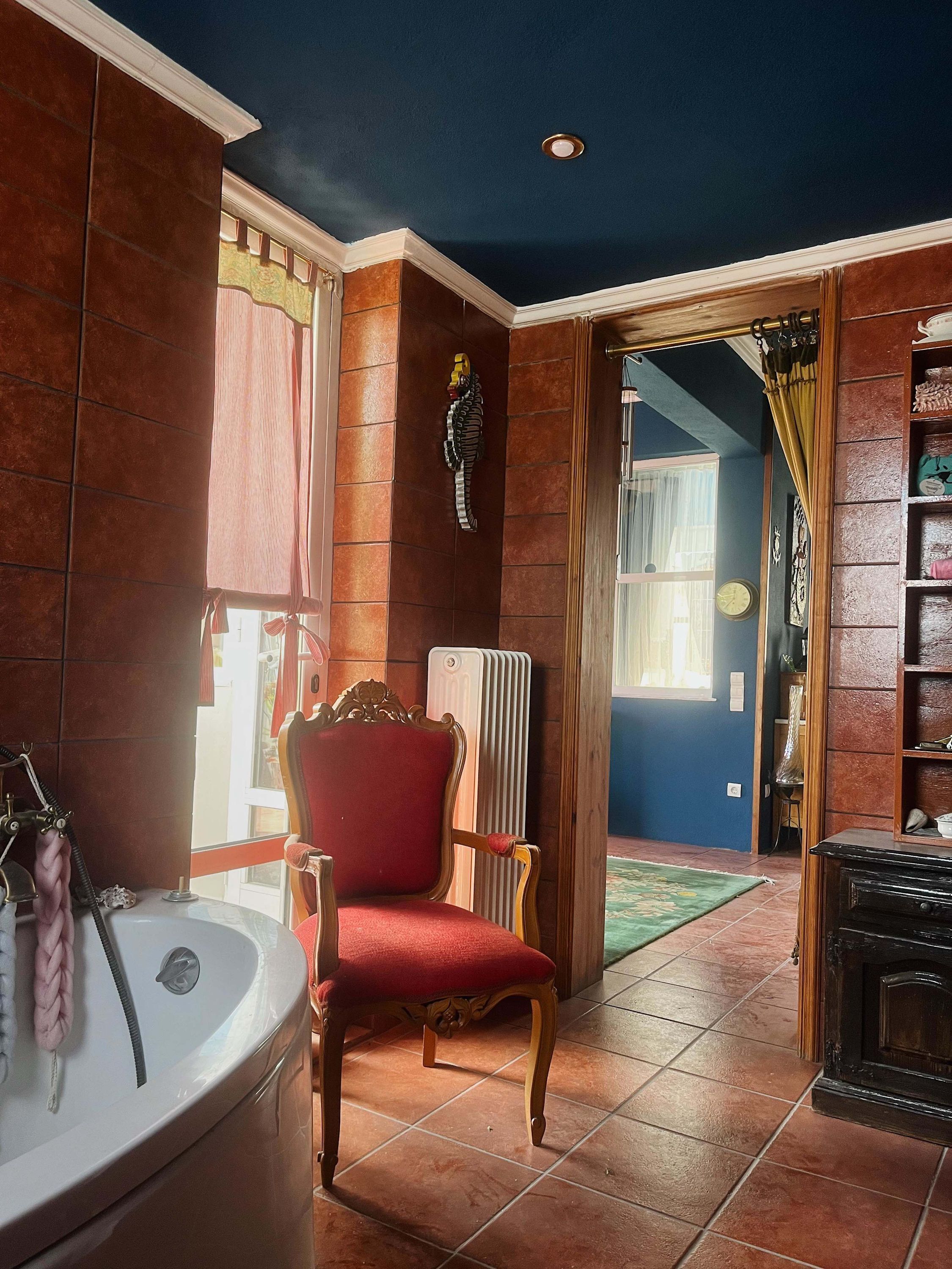 A bathroom with a bathtub, a red chair, a radiator, and a bookshelf.