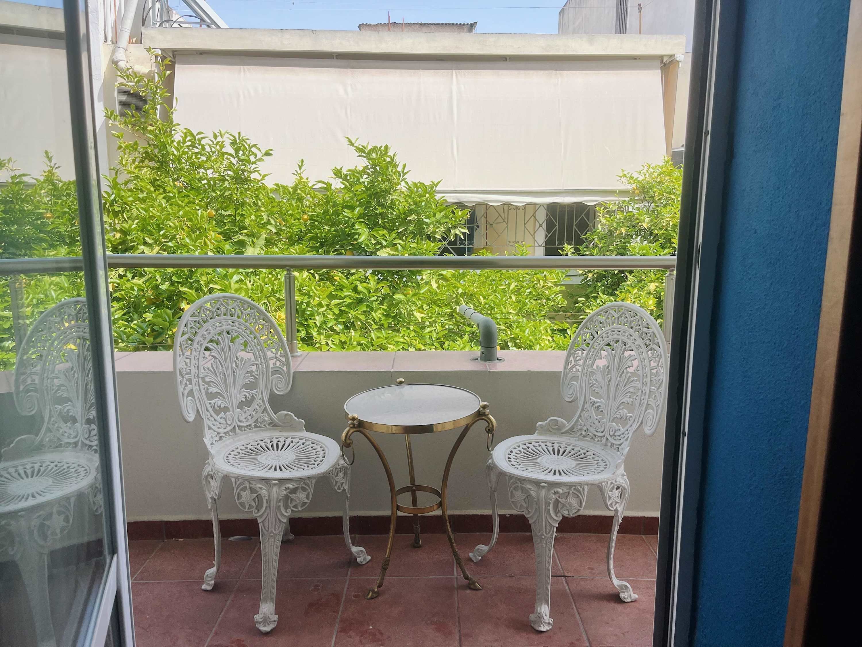 Un balcon agrémenté de deux chaises blanches décorées et d’une petite table ronde, le tout entouré d’une rambarde en métal.