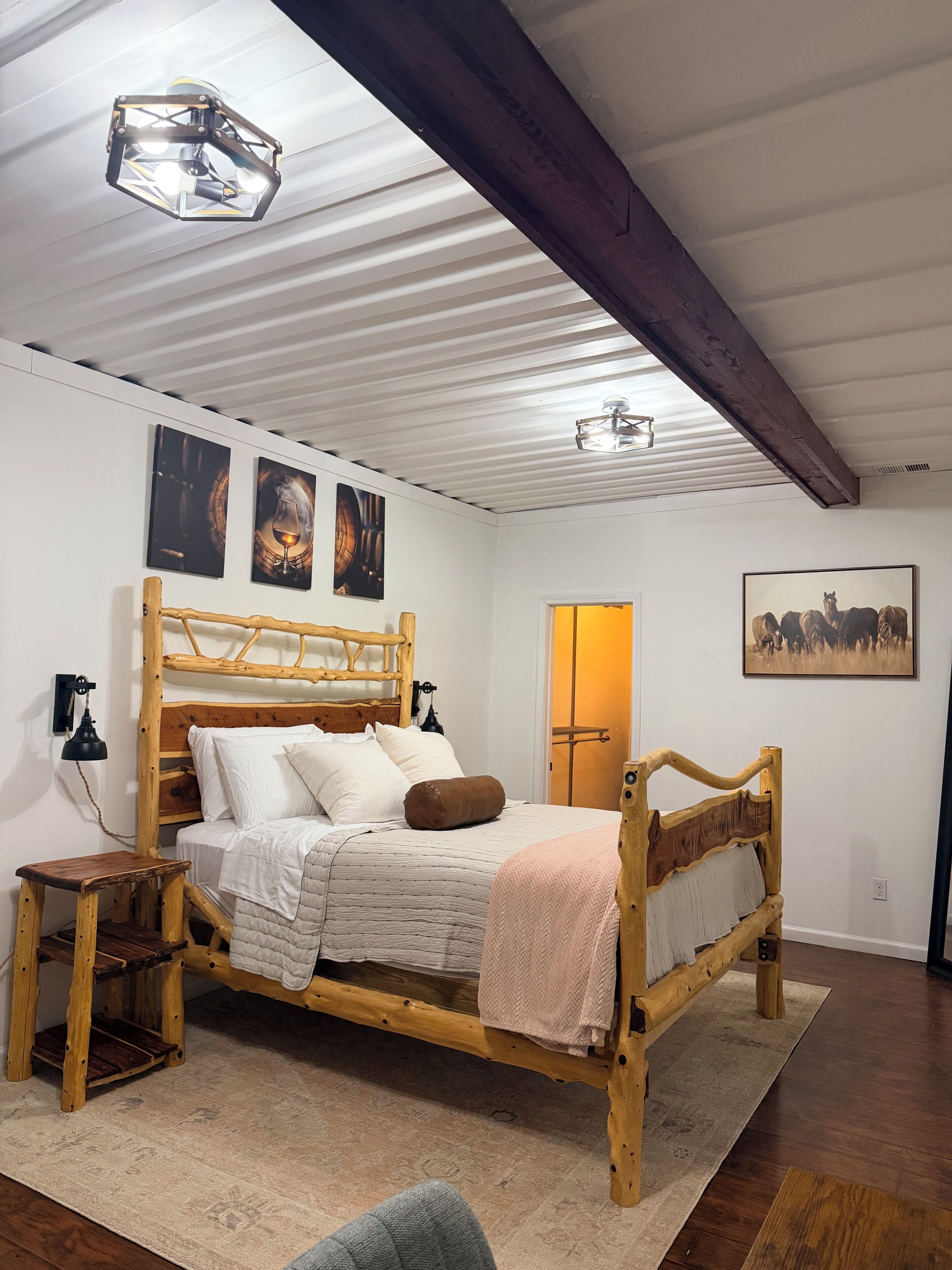 Un letto di legno con testiera, un comodino, una lampada e un tappeto in una stanza con pareti bianche e soffitto spiovente.
